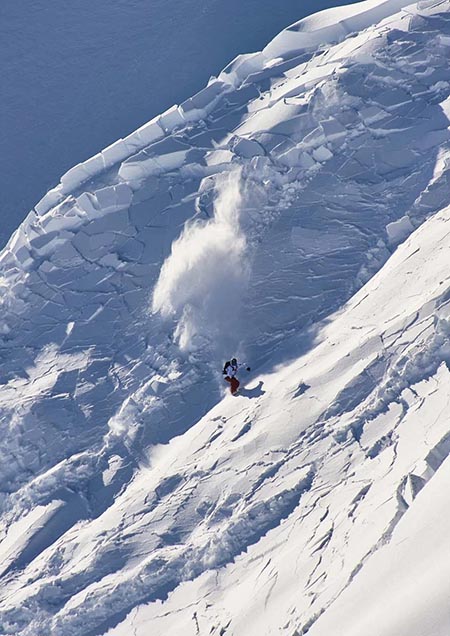 A snowboarder in red pants and a white jacket on a steep slope of snow that is breaking apart