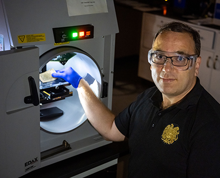 Researcher stands in front of a large machine, holding the delicate money inside.
