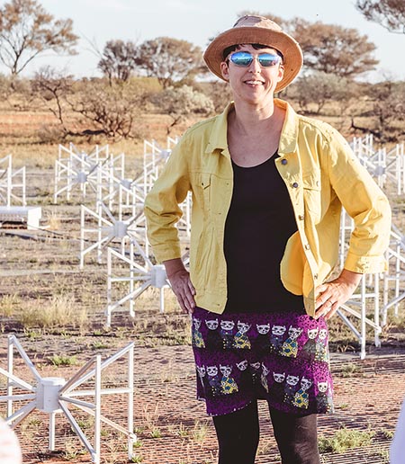 Natasha Hurley-Walker stands outside in front of short radio telescope components in an arid landscape.