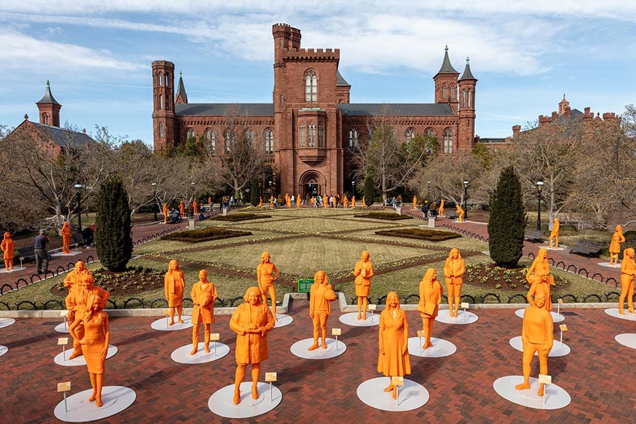 Orange statues on display in front of a large brick building.