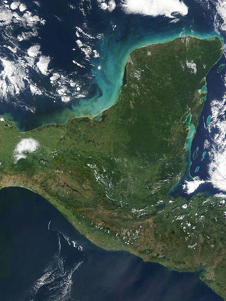 Photograph of the Yucatán penninsula taken from space showing a green landmass, blue ocean, and white clouds