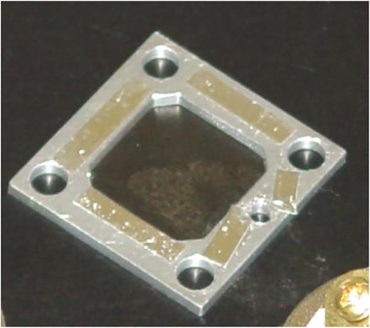 Handmade charge-control mesh-screen. 25 × 25 mm aluminum square (0.8 mm thick) with a 90% transparent nickel metal mesh taped down by hand using aluminum tape to one side of the square. Holes allow screws to be used if clips are not available. The mesh-screen itself is not perfectly flat. To produce a flat electric field, the aluminum needs to be grounded. Depending on the sample thickness, other mesh-screens or spacers were built using 0.5, 1.0, 1.5, and 2.0 mm thicknesses.