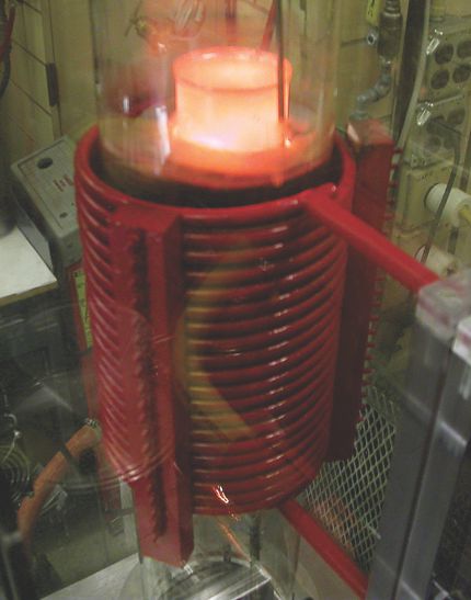 . A vacuum induction furnace at Ames Lab being used to distill a rare-earth metal. The red induction coil surrounds a quartz vacuum tube. The glowing cylinder at the top is the condenser, which collects the metal.