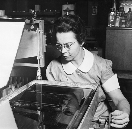 Figure 4. Katharine Blodgett (1898–1979), photographed in 1938, demonstrates an early version of the Langmuir–Blodgett trough. Turning a hand pulley repeatedly dips the glass slide into a solution of fatty acids on the surface of a water bath. The dips coat the glass with successive monolayers. (Imagefrom the Smithsonian Institution Archives.)