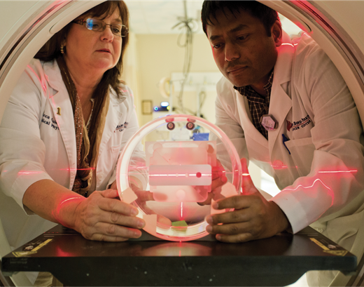 Medical physicist Becky Guidry (left), of the Mary Bird Perkins Cancer Center in Baton Rouge, Louisiana, shows trainee Bijoyananda Adhikary how to work with a quality assurance device being used on a diagnostic CT scanner. The images taken by this CT scanner will help in planning computer-optimized radiation therapy that employs x rays or electrons.