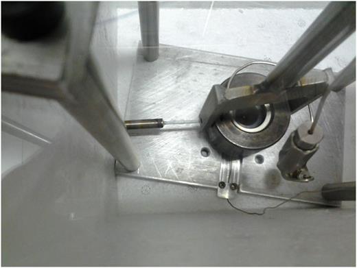 FIG. 2. Top view of the “spray-loading” apparatus before the use. The deposition capillary coated with the Teflon® tape and passing through the dedicated opening on the DAC cover is clearly visible, together with the fork for DAC mechanical closure and the thermocouple wire passing through its dedicated channel milled on the DAC holder. In the picture, the Nova-Swiss® adapter that connects the “membrane side” of the DAC, with its microvalve, to the external pressure driving system through a 1/16 in. stainless steel high-pressure capillary is also visible.